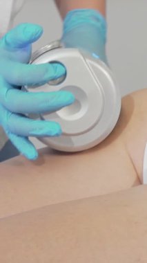 Büyüleyici bir yakın çekim, yetenekli bir güzellik uzmanının, eldivenli bir eldiveni bir kadının kalçasının üzerinde ustalıkla manevra yaparak selüliti azaltma amaçlı gençleştirici bir masaj yaptığını gösteriyor. Güzellik salonunun sakin atmosferi