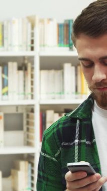 Renkli kitaplarla dolu dinamik bir kütüphanede, koyu saçlı ve cep telefonuyla sohbet ederken zevkten dört köşe olan genç bir adam. Kareli yeşil tişörtü beyaz bir tişörtün üzerine giyince coşku ve motivasyon yayıyor.