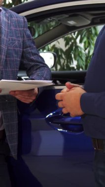 İki şık giyinmiş adam, biri şık bir ceket giymiş, diğeri ise gevrek mavi gömlekli, anlaşmayı imzaladıktan sonra zevkle el sıkışıyorlar. Bu dinamik an profesyonelliği ve memnuniyeti yansıtıyor.