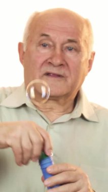 Sıcak bir gülümsemesi ve gri saçları olan neşeli bir son sınıf öğrencisi neşeyle kabarcıkları üflüyor, havayı neşe ve neşe ile dolduruyor. Enerjisi mutluluk saçıyor. Emeklilikteki kaygısız anların ve basit sevinçlerin özünü yakalıyor.