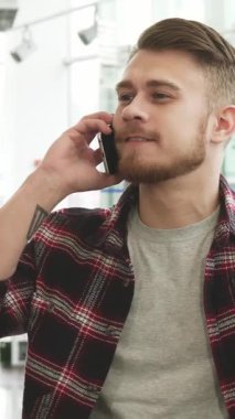 Zarif bir ekose gömlek giyen neşeli, sakallı genç bir adam şık bir araba galerisinde animasyon bir telefon görüşmesi yapıyor. Kendine güvenen gülüşü ve parlak gözleri araba alışverişinin heyecanını yansıtıyor.