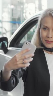 Işıl ışıl bir kadın, modern bir galeride parlak ve şık araçlarla çevrili yeni araba anahtarlarıyla selfie çeker. Heyecan ve kutlamalarla dolu bu canlı sahne, heyecan verici otomotiv yolculuğuna çıkarken zevkini vurguluyor.