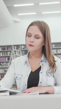 Büyüleyici düşük açılı bir çekimde, modern bir kütüphanede özenle notlar alırken kaşı konsantrasyonunu bozan çekici genç bir kız öğrenci sergileniyor. Etrafı renkli kitaplarla dolu raflarla çevrili, öğrenmeye olan bağlılığı...