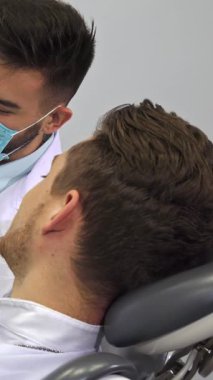 Parlak bir diş kliniğinde, beyaz önlüklü, yetenekli, sakallı bir dişçi ayrıntılı bir model kullanarak insan dişlerinin karmaşık düzenini tutkuyla gözler önüne seriyor. Şık bir saç kesimi olan özenli erkek hasta, anlayışla başını sallar.