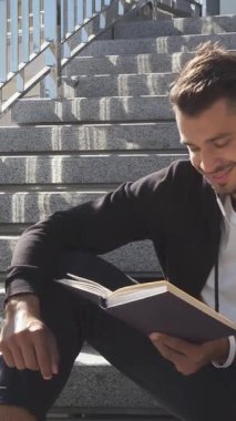 Koyu renk saçlı ve sakallı dingin bir genç adam güneşli şehir merdivenlerinde rahatça oturuyor, kitabına dalmış bir şekilde. Yanında ferahlatıcı bir şişe suyla canlı şehir manzarasının ortasında sükuneti somutlaştırarak mükemmel bir karışım yaratıyor.