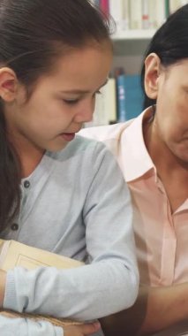 Işıldayan olgun bir Asyalı kadın, canlı raflarla dolu samimi bir kütüphanede renkli bir kitaba bakarken meraklı küçük kızıyla keyifli bir anı paylaşıyor. Bu iç açıcı sahne aile bağlarının özünü güzel bir şekilde gösteriyor.