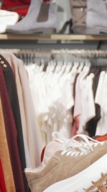 Canlı bir perakende arkaplanı arasında şık bir çift spor ayakkabısı tutan, kameraya dalgalı saçlar saçı olan ışıl ışıl genç bir kadın. Bir dizi şık kıyafetle çevrelenmiş bir şekilde, bir alışveriş macerasının heyecanını yakalıyor,