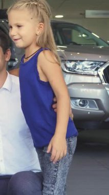 Memnun bir baba kızının yanında diz çöker. İkisi de modern bir galeride göz kamaştırıcı kırmızı bir arabayı keşfederken heyecan saçar. Baba nazikçe arabaları okşar, tampon süsler, kahkahaları ve şakaları paylaşır, içten bir aile yaratır.