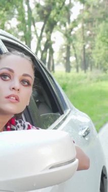 Çarpıcı genç bir kadın, sakin kırsalın canlı yeşilliğini emerken derin düşüncelere daldığı ifadesini yansıtan zarif bir şekilde arabasının camından dışarı sarkıyor. Bu büyüleyici sahne macera ve özgürlüğün özünü yakalıyor.