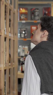 Şık bir süveter giyen genç bir adam hareketli bir pazarda duruyor, dikkatle raflardaki renkli şarap şişelerini inceliyor. Bu büyüleyici sahne keşfin heyecanını ve her şenlik için ideal şarabı seçmenin hazzını yansıtıyor.