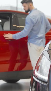 İyi bakımlı sakallı şık bir genç adam şık bir otomobil bayisinde çarpan kırmızı bir arabayı inceliyor. Sahne heyecan ve entelektüellik saçıyor, arabaları gösterişli bir şekilde bitiriyor ve modern sergi salonlarının parlak ambiyansını sergiliyor.