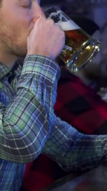 Yakışıklı, kahverengi saçlı bir adam neşe saçıyor. Kahkaha ve gevezelikle dolu bir barda buzlu bira bardağını gururla kaldırıyor. Bu şık beyaz erkek, modaya uygun bir tişört giymiş, kutlama ve dostluk ruhunu temsil ediyor.