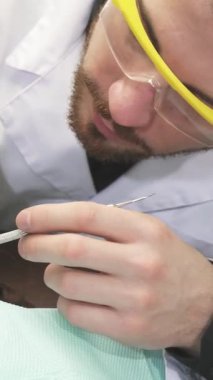 Parlak, modern bir diş hekiminde, koruyucu gözlük ve beyaz önlük takan kendini işine adamış bir dişçi, nane yeşili, rahat bir dişçi koltuğunda oturan sakin genç bir kızın üst dişlerini dikkatle inceler. Yumuşak atmosfer kızlar tarafından arttırılır.