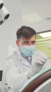 Modern, el değmemiş bir dişçi kliniğinde, kendini dişlerine adamış bir erkek dişçi küçük bir kızın dişlerini dikkatle inceleyerek, dişlerini hassasiyetle kontrol eder. Parlak, steril çevre, dişçilerin nazik yaklaşımıyla birleşince,