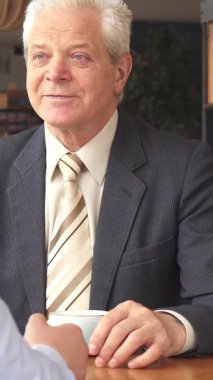 Sıcak ışıkla dolu büyüleyici bir kafede, iki Kafkasyalı iş ortağı buluşmalarını sonlandırıyor, dostluk ve profesyonellik yayıyorlar. Yaşlı, gri saçlı bir adam, doğmakta olan meslektaşıyla tokalaşırken zevkten dört köşe olur.