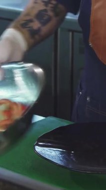 Canlı bir mutfakta, şık bir önlük ve eldiven giyen yetenekli bir şef, renkli taze sebzeleri parlak siyah bir tabağa ustalıkla aktarıyor. Bu büyüleyici an gurme yemek hazırlama sanatını vurguluyor.