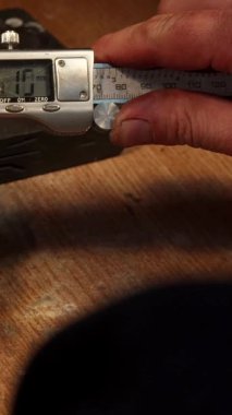 Kafkasyalı bir kuyumcu titizlikle zirkon taşlarını dijital kalibre ile titizlikle ölçerek hassasiyetini ve sanatını vurgular. Becerikli elleri aletleri, göz kamaştırıcı bir şekilde çevrelenmiş ahşap bir tezgahın üzerinde nazikçe manipüle ediyor.