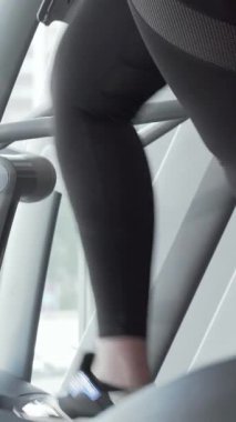 Şık, forma uygun spor kıyafetleri içinde canlı, iri yarı bir kadın eliptik bir eğitmen üzerinde enerjik bir şekilde çalışıyor, pozitiflik ve kararlılık yayıyor. Yakın çekim onun neşeli yüz ifadesini ve egzersiz hareketlerini vurguluyor.