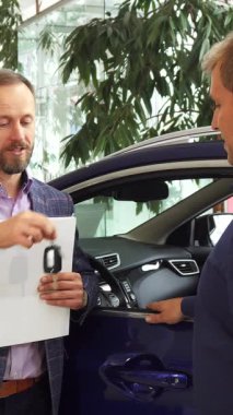 Gösterişli, modern bir araba galerisinde, ışınlama satıcısı hem neşe hem de memnuniyet saçan yeni sahibine anahtarları teslim eder. Şatafatlı araçlar ve verimli yeşilliklerle çerçevelenmiş sıkı tokalaşmaları başarılı bir alışverişi simgeliyor.