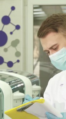 El değmemiş beyaz önlük ve mavi lateks eldivenler giyen genç erkek laboratuvar asistanı, test sonuçlarını canlı sarı bir klasörde dikkatlice belgeliyor. Etrafı son teknoloji laboratuvar ekipmanları ve renkli moleküler grafiklerle çevrili.