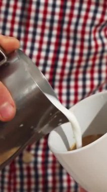 Şık, kareli gömlekli yetenekli genç bir adam kapuçinonun üstünde çarpıcı bir kalp tasarımı yapan beyaz bardağa hassasiyetle buğulanmış süt döker. Bu büyüleyici an, tutku ve yeteneğin harmanlandığı latte sanatının özünü yakalıyor.