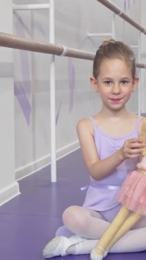 Bu büyüleyici uzunluktaki çekim neşeyle el sallayan küçük bir balerinin etek giymiş bebeğini sallamasını içeriyor. Canlı bir bale stüdyosunun arka planında leylak rengi taytlı ve yumuşak taytlı sevimli bir kız...