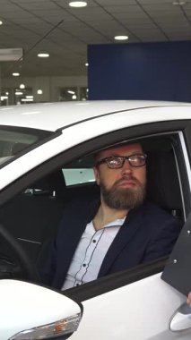 El değmemiş beyaz bir hatchback 'in içinde, keskin siyah takım elbiseli şık bir satış müdürü, sözleşmenin detaylarını tutkulu bir şekilde odaklanmış bir müşteriye açıklar. Sakallı adam, özgüven saçıyor, dikkatle dinliyor, güven dolu profesyonel bir atmosfer yaratıyor.