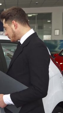 Özel dikim siyah takım elbiseli dengeli bir satış müdürü galerideki beyaz bir hatchback 'in içindeki bir müşteriyle sözleşmenin detaylarını tutkuyla tartışıyor. Çekici sakallı adam dikkatle dinliyor, profesyonellik atmosferini teşvik ediyor ve