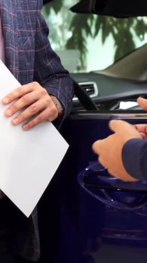 Canlı bir araba galerisinde, heyecanlı bir adam şık giyimli bir satıcıdan yeni aracının anahtarlarını zevkle kabul eder. Sıkı tokalaşmaları başarılı bir alışverişin özünü yakalar. Heyecan ve memnuniyet saçar.