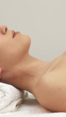 Çekici esmer bir kız, yumuşak beyaz bir havluya sarılı bir masaj masasına uzanmış, huzurlu spa ortamını aydınlatan ışıl ışıl gülüşü. Bu çekici beyaz kadın model yüzünü kameraya doğru çeviriyor, rahatlamanın vücut bulmuş hali.