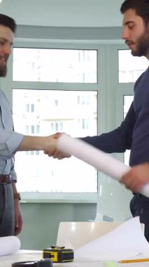 Gösterişli, güneşli bir ofiste, iki genç erkek mimar hevesle el sıkışıyor, başarılı işbirliklerini sağlamlaştırıyorlar. Tarz sahibi beyaz tasarımcılar, detaylı planlar ve canlı turuncu bir başlıkla çevrelenmiş, profesyonellik saçıyorlar.