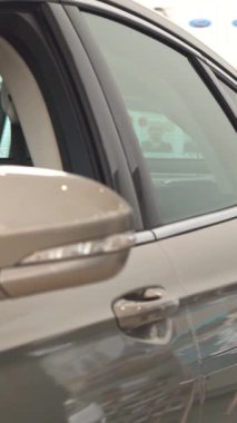 Zarif sakallı ve gözlüklü çekici bir beyaz adam parlak gri bir sedanı incelemek için eğildi ve onayladı. Kendine güveni ve keskin iş elbisesi modern galeride heyecan saçıyor.