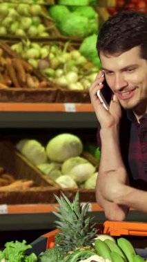 Şık, esmer bir adam canlı alışveriş arabasının üzerine yaslanır, neşeli bir telefon görüşmesi yapar ve renkli taze ürünlerle çevrilidir. Sıcak gülüşü ve rahat tavırları davetkar bir atmosfer yaratıyor.