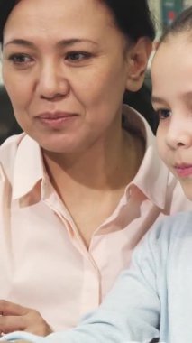 Neşeli küçük bir Asyalı kız ve özenli annesi renkli kitaplarla dolu samimi bir kütüphanede gülümseme ve bilgi paylaşıyorlar. Bu yürek ısıtan an aşkın ve aşkın bağını güzel bir şekilde gösteriyor.