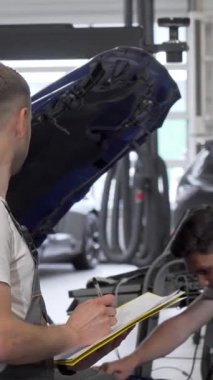 Alet ve araçlarla dolu canlı bir garajda, kendini adamış iki tamirci bozuk bir otomobili tamir etmek için odaklanmış bir diyaloğa giriyorlar. Bir erkek teknisyen, asistanı motoru incelerken not defterine titizlikle not alıyor.