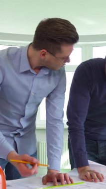 Doğal ışıkla dolu parlak, havadar bir ofiste, iki beyaz mimar bir inşaat projesinde dinamik bir işbirliği içinde, yüzleri coşkuyla ışıldıyor. Şık gözlükler takan bir adam mimari planları dikkatle ölçüyor.