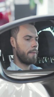 Zevkli bir genç adam, lüks arabasının parıldayan yan aynasında arabanın anahtarlarını tutarken gururla ışıldıyor. Bu kendine güvenen iş adamı, şık bir sakalı ve parlak bir gülümsemesi olan, modern bir sergi salonunda başarı ve neşeyi somutlaştırıyor.