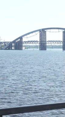 Büyüleyici bir nehir kenarı sahnesinde uzun siyah saçlı at kuyruklu genç bir kadın, sakin manzaranın tadını çıkarırken boynunu havluyla siliyor. Şık bir menekşe kazak giyip, kulaklıklarıyla müzik dinliyor.