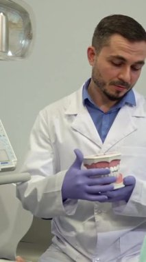 Yetenekli bir esmer beyaz dişçi ayrıntılı bir diş modeliyle dişlerinin düzenini büyük sarışın müşterisiyle çatışarak büyük bir hevesle gösteriyor. Modern klinik, son model diş malzemeleriyle donatılmıştı.