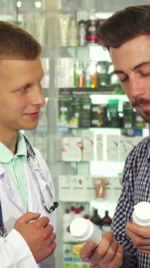 Aydınlık ve davetkar bir eczanede, beyaz önlüklü bir erkek doktor iki ilaç şişesini düşünceli bir şekilde karşılaştıran bir hastayla karşılaşır. Sahne profesyonellik ve samimiyet yayarak, kişisel tercihlerin hayati önemini vurguluyor.