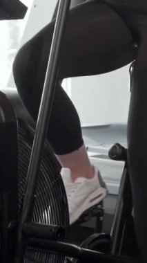 Kendine güvenen kıvrımlı bir kadın, spor salonundaki hava bisikleti üzerinde güçlü bir şekilde pedal çevirirken, spor yapmaya olan bağlılığını gösteriyor. Parlak, enerjik çevre, doğal ışıkla dolu, vücudunun pozitifliğini ve kararlılığını arttırıyor.