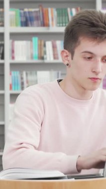 Yumuşak pembe kazaklı kendini adamış genç bir erkek öğrenci yoğun bir şekilde laptopuna odaklanmış, renkli ciltlerle dolu canlı kitaplıklarla çevrili. Sınavlara hazırlanırken, modern teknolojiyi kusursuz bir şekilde harmanlayarak konsantrasyonu yayılıyor.