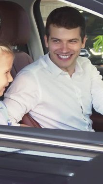 Gösterişli, modern bir aracın içinde, keyifli bir baba, büyüleyici bir menekşe elbise giymiş meraklı kızına çeşitli araba özellikleri sergiliyor. Paylaştıkları gülücükler ve ışıl ışıl gözler aile tablosu oluşturuyor.