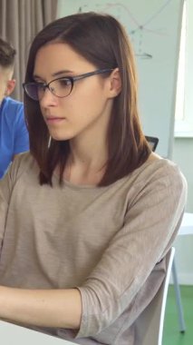 Kendine güvenen esmer bir kız, parlak, modern bir ofis masasında parlak bir dizüstü bilgisayarında yazı yazarken baş parmağıyla ışıldıyor. Canlı arkaplanda, takım çalışması ve yaratıcılıktan oluşan bir atmosfer yayarak heyecanlı bir tartışmada üç katılımcı yer alıyor.