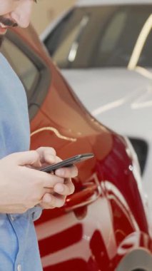 Şık sakallı neşeli bir adam akıllı telefonuyla mesajlaşır. Canlı bir galeride çarpan kırmızı bir arabaya yaslanır. Işıldayan araçlarla dolu parlak sergi salonu heyecan verici bir atmosfer yayıyor.