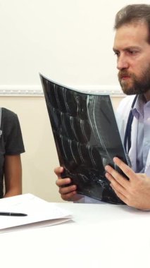 Güneşli bir ofiste, sıcak bir gülümsemesi olan genç bir erkek doktor neşeyle bir reçete yazıyor, şefkat ve profesyonelliği somutlaştırıyor. Beyaz önlüğü ve steteskobu hasta bakımına olan bağlılığını yansıtıyor.