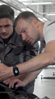 Gösterişli gri üniformalar içinde iki oto tamircisi açık bir arabanın kaputuna yaslanmış, karmaşık bir motor sorunu teşhisi koyuyor. Odaklanmış ifadeleri ve işbirlikçi ruhları, otomotiv başarısını sağlayan hayati takım çalışmasını aydınlatıyor.