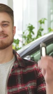 Şık sakallı, gururlu genç bir adam lüks ve modern bir bayilikte araba anahtarlarını elinde tutarken neşe saçıyor. Arkasındaki pırıl pırıl araç onun heyecan verici yeni sahiplik macerasını temsil ediyor, otomotiv rüyalarının heyecanını özetliyor ve