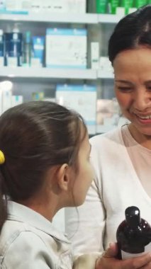 Renkli sağlık ve güzellik ürünleriyle dolu canlı bir eczanede, keyifli bir anne, bir ilacı birlikte incelerken meraklı kızıyla özel bir anı paylaşıyor. Küçük kız, uzun siyah saçları arkadan bağlanmış ve parlak bir gülümsemesi vardı.