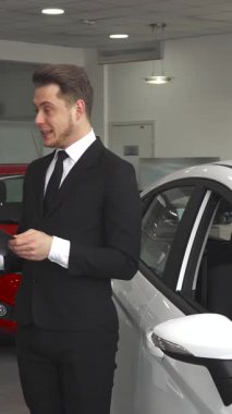 Gösterişli siyah bir takım elbise içinde, kendine güvenen bir satış müdürü modern bir araba galerisindeki bir müşteriye sözleşmenin detaylarını hevesle açıklar. Genç Kafkasyalı danışman, parlak beyaz bir araca doğru hareket ederek, onun özelliklerini vurgular,